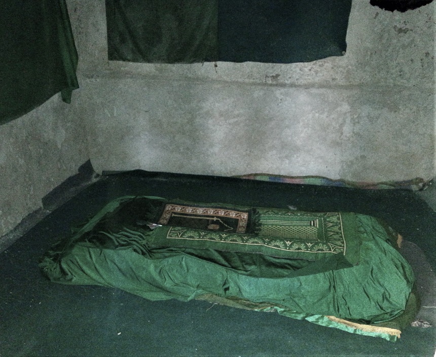 Inside a Persian domed tomb (ziyarat) on Qeshm Island, showing a resting bed covered with a colorful, handcrafted duvet.