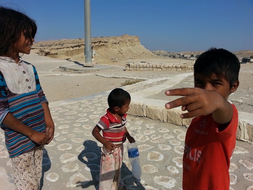 Three local children—a girl and two boys—standing among the historical ruins of Qeshm Island, Iran.